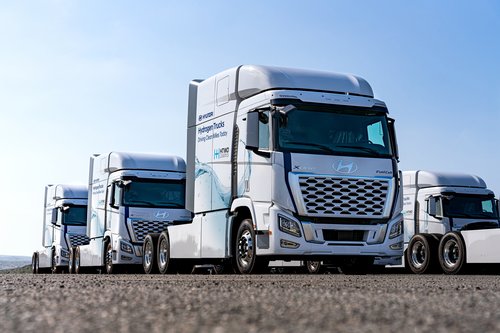 A line of Hyundai XCIENT fuel cell trucks, showing the words "Hydrogen Trucks Driving Clean Miles Today" on the side.